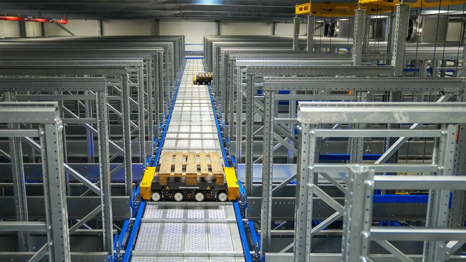 A pallet shuttle carrying a wooden pallet along its rail between tall rows of steel racking.