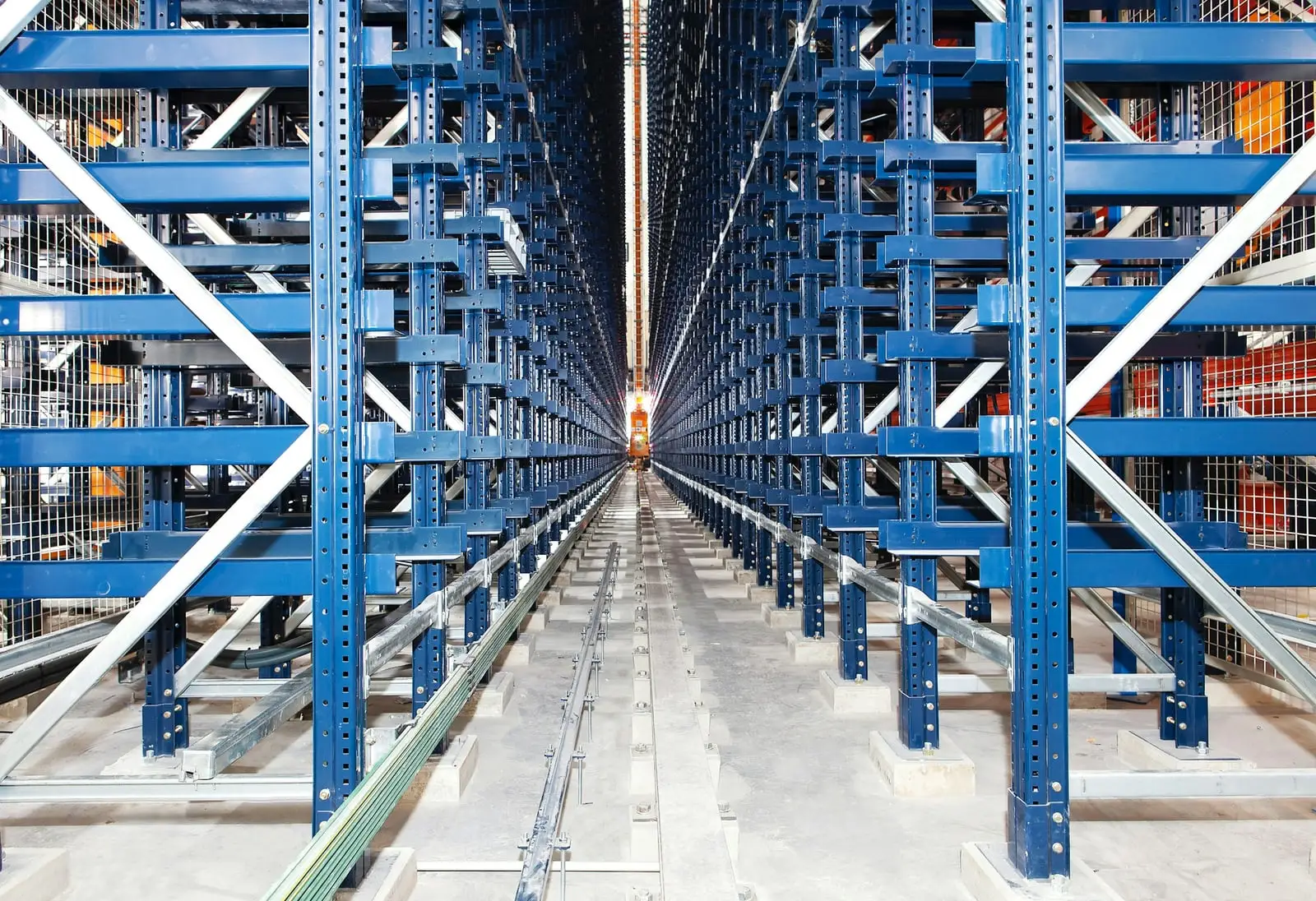 A long, narrow aisle between very tall blue steel racks, with a rail running down the middle of the floor.